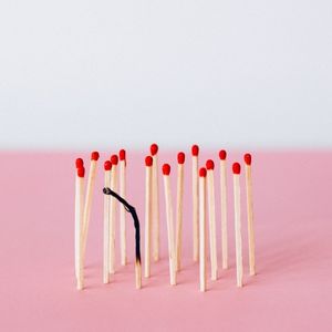to represent burnout an image of several unlit matches are standing upright on a pink surface. One of the matches has burned down.